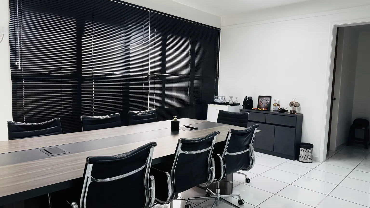 Sala ampla do andar com mesa de reunião e persianas escuras na fachada envidraçada